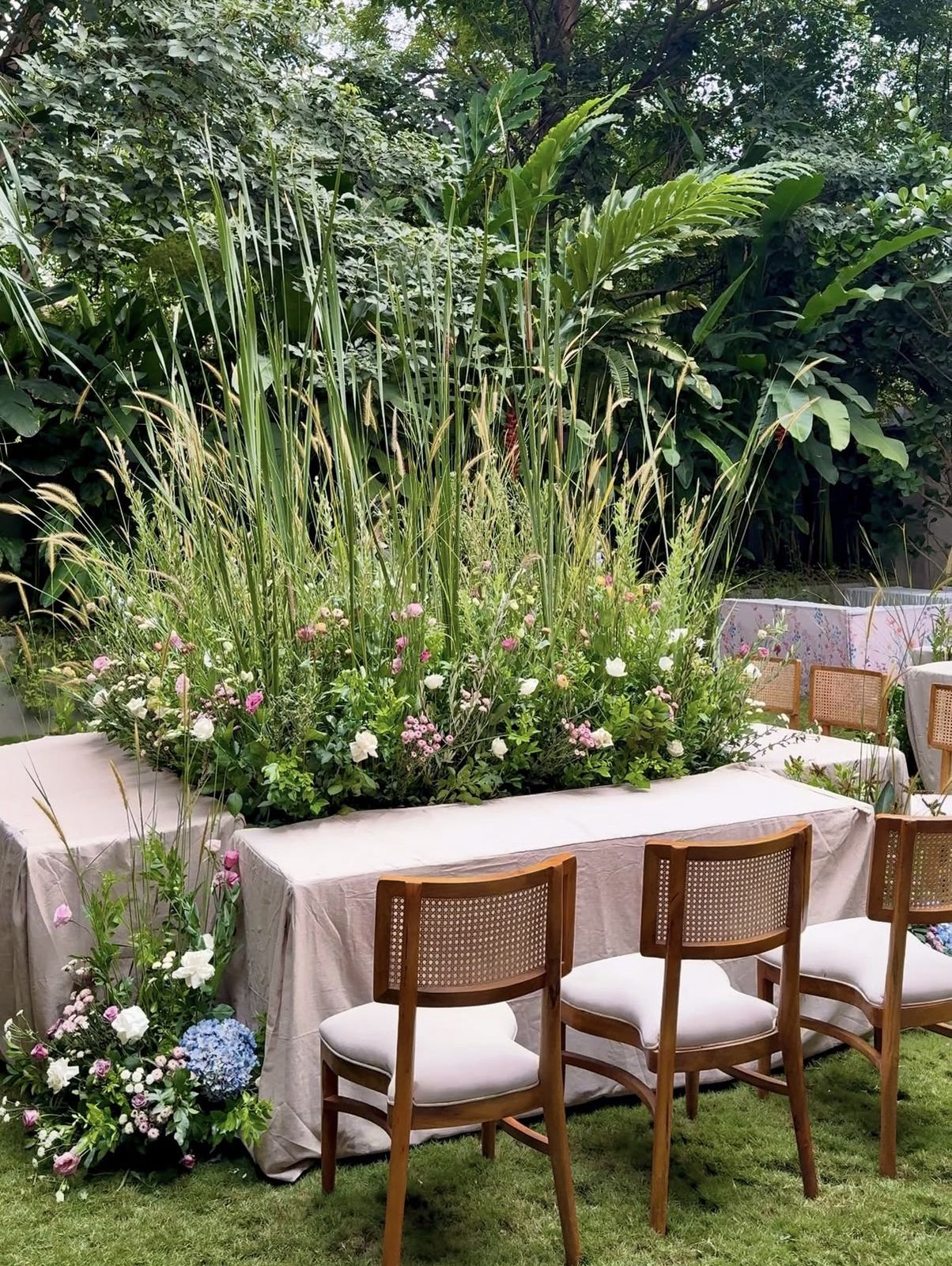 Long garden table with a meadow of tall grasses and wildflowers and cane chairs